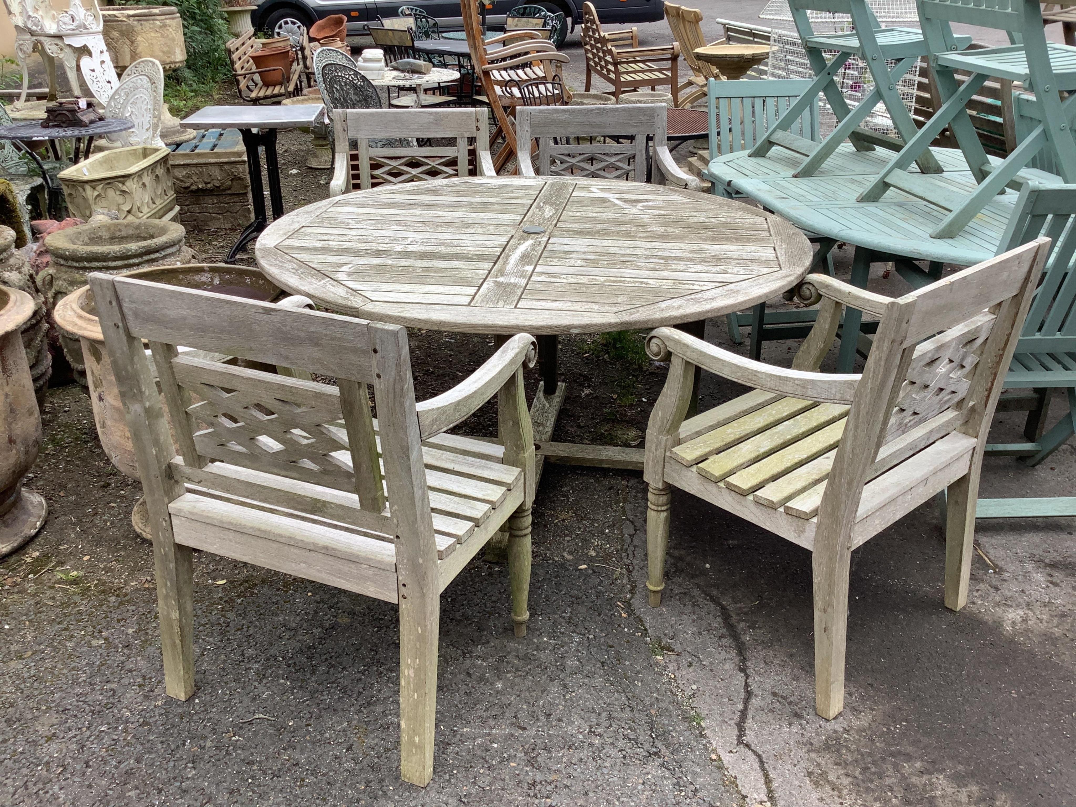 A circular weathered teak garden table, width diameter 150cm, height 73cm and four elbow chairs